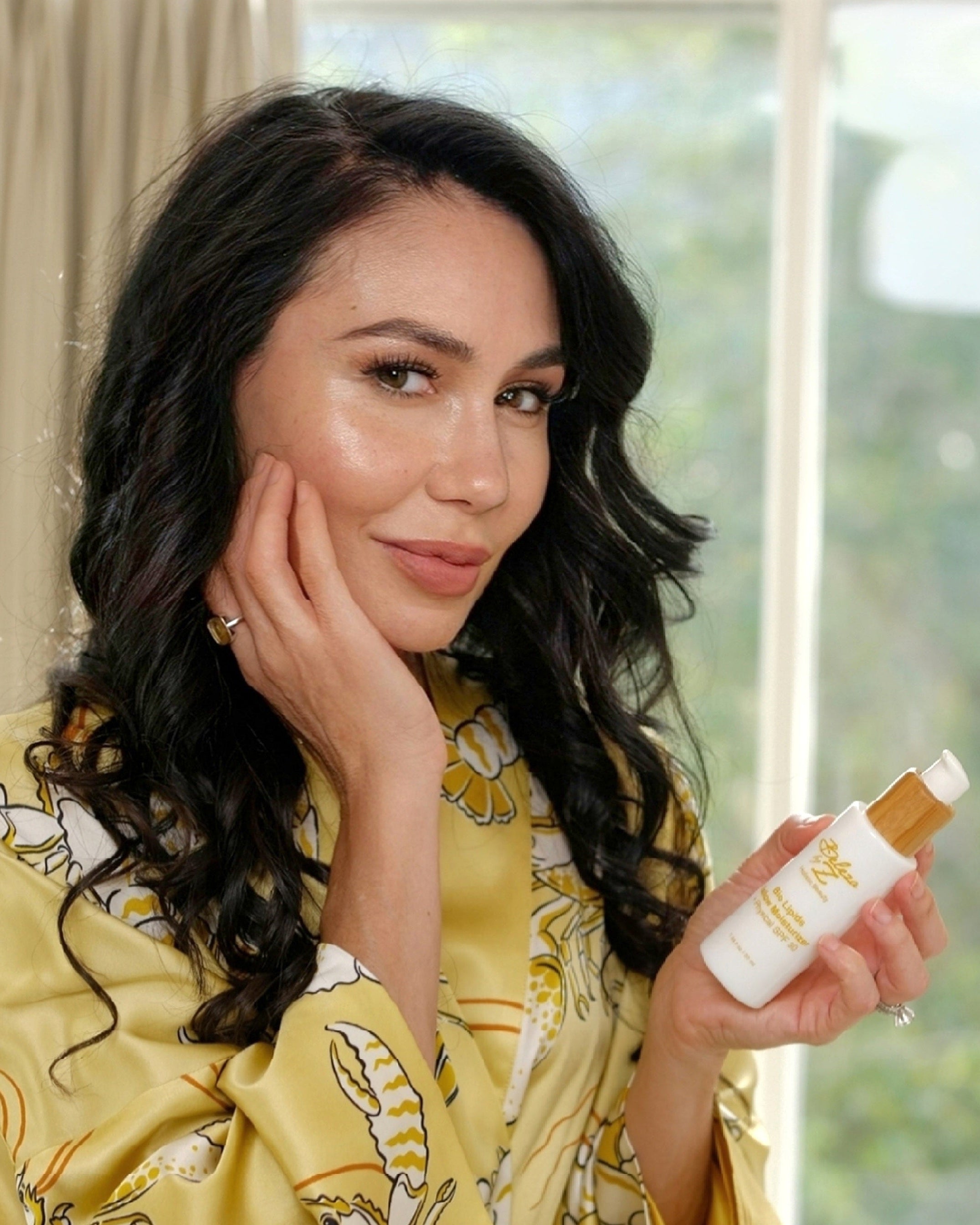 A model holding a bottle of Beleza by Z tallow skincare moisturizer in a luxurious bathroom vanity setting. 