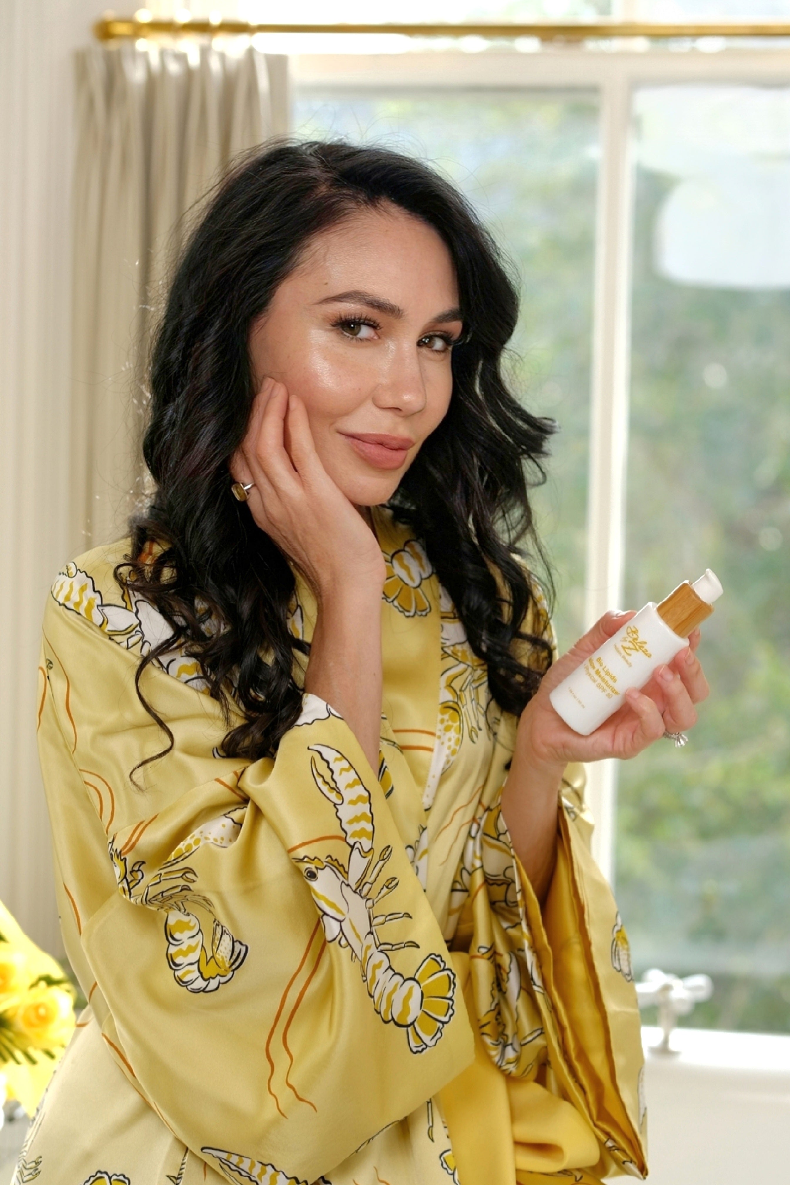 A model holding a bottle of Beleza by Z tallow skincare moisturizer in a luxurious bathroom vanity setting. 